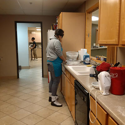 young woman is blindfolded, standing at kitchen counter with various bowls and cooking ingredients before her