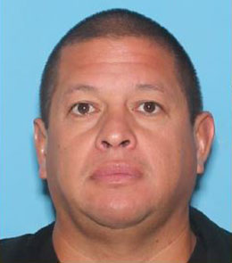 A Hispanic man with buzzed, brown hair, and brown eyes is wearing a black polo shirt