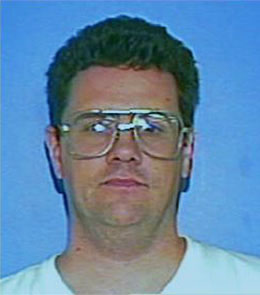 A Caucasian man with brown eyes and short, brown hair is wearing large glasses and a white t-shirt