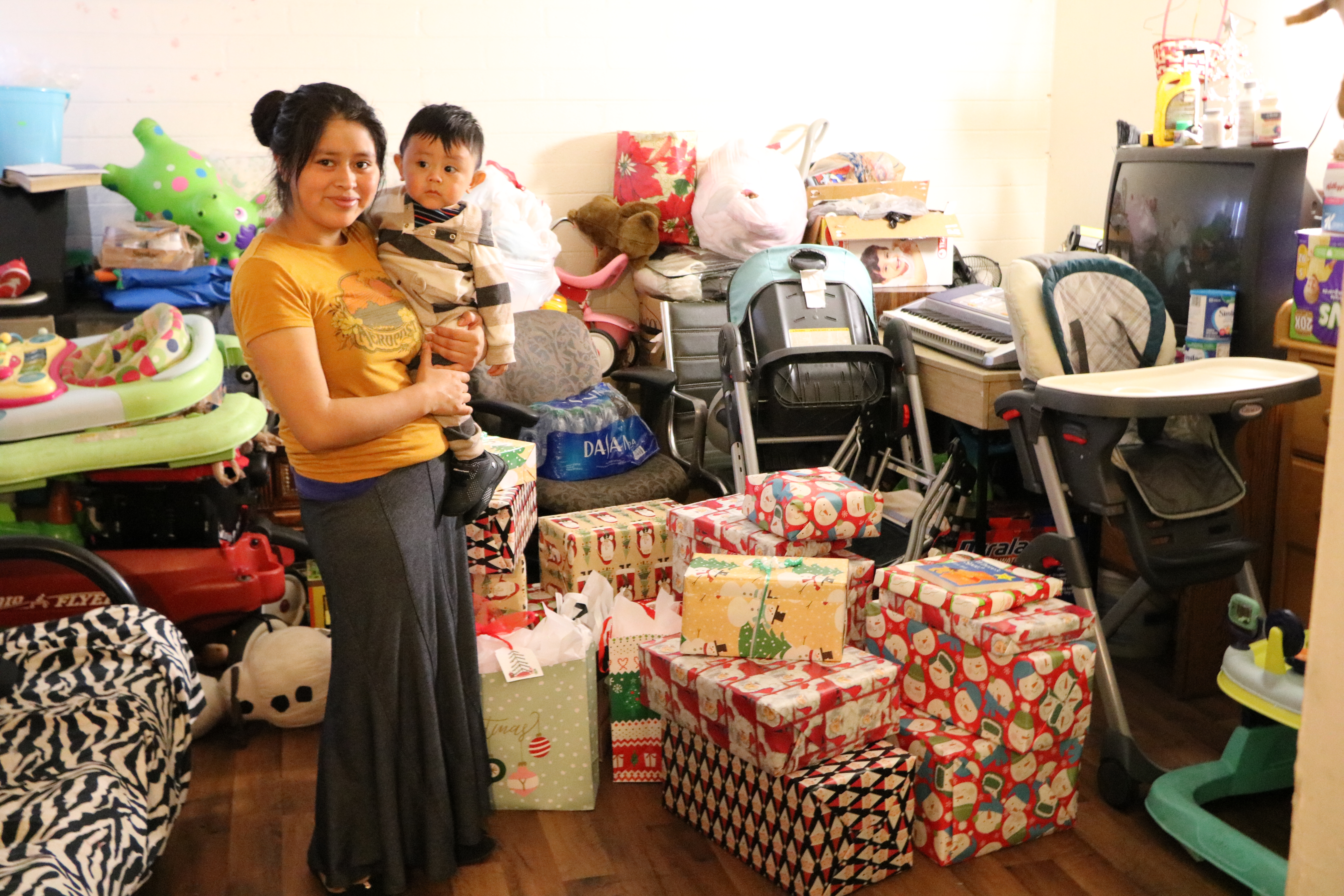 Mother and toddler stand in front of a pile of wrapped gifts