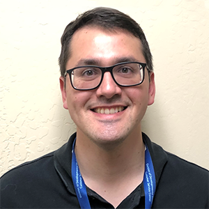 a man brown-haired man wearing glasses and a black polo shirt is smiling