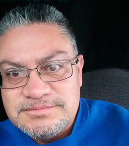Hispanic male with brown eyes, graying black hair and goatee is wearing glasses
