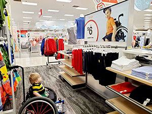 inside a clothing storye, a little boy in a wheelchair looks up at a poster of a boy who is also in a wheelchair