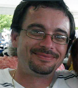 A White male with brown eyes, brown hair, mustache and goatee, wearing glasses.