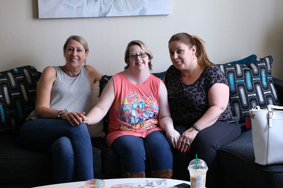 On the living room couch, a young woman sits between her mother and a woman who mentors her.