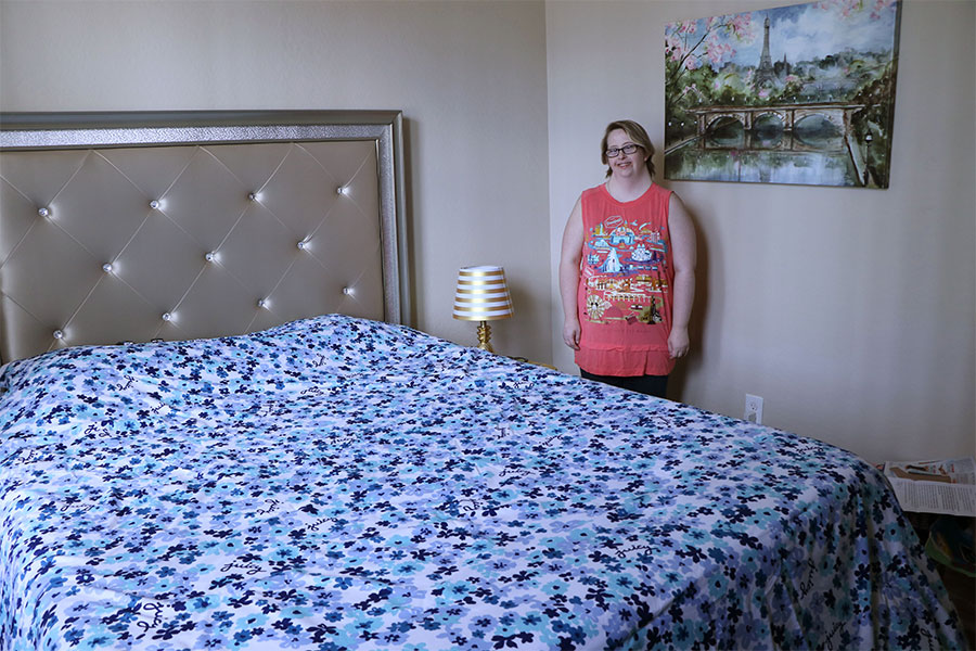 Young woman stands to the side of her bed in her Parisian decorated bedroom.