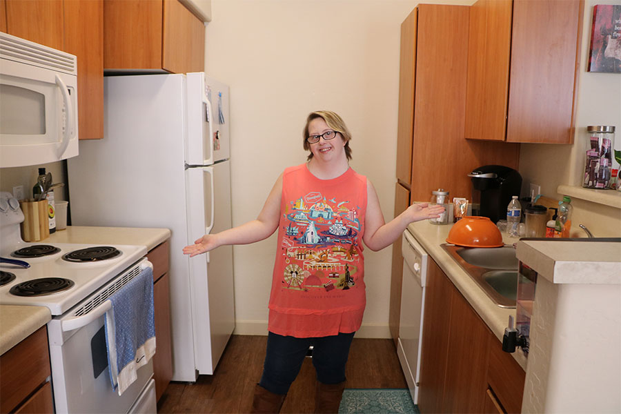 Young woman expands her arms out to showcase her kitchen.