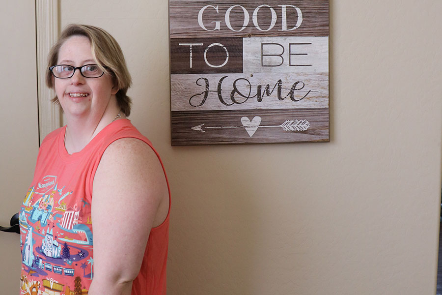 Young woman stands by wall art that reads:  It is so good to be home.