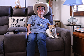 Woman wearing a cowboy hat sits on her couch at home with her dog