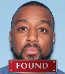 A black man with buzzed black hair, brown eyes, and a mustache with a beard