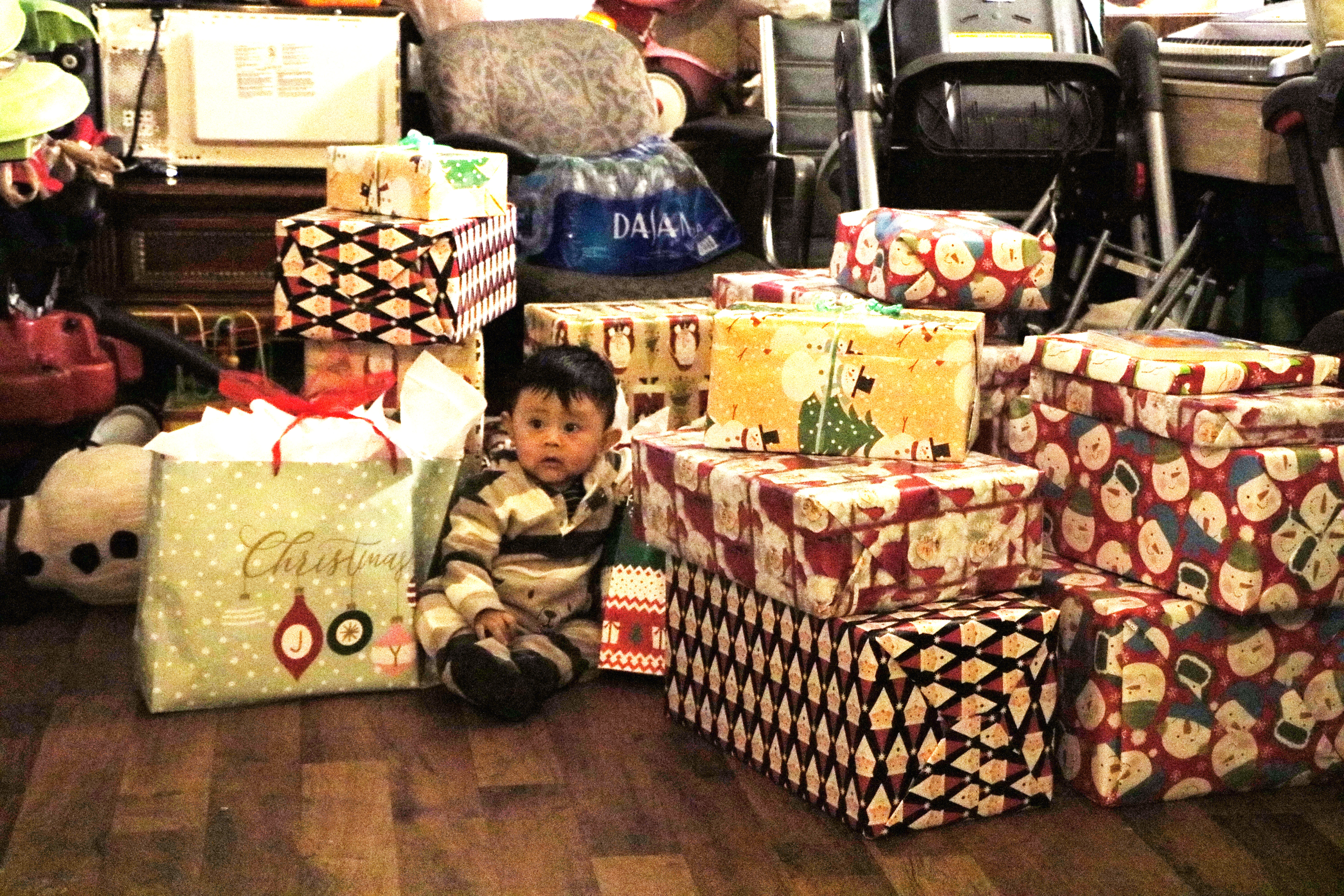 Toddler sits on floor among a stack of holiday presents