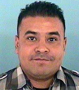 A Hispanic man with short, spiked, black hair and brown eyes is wearing a plaid shirt.