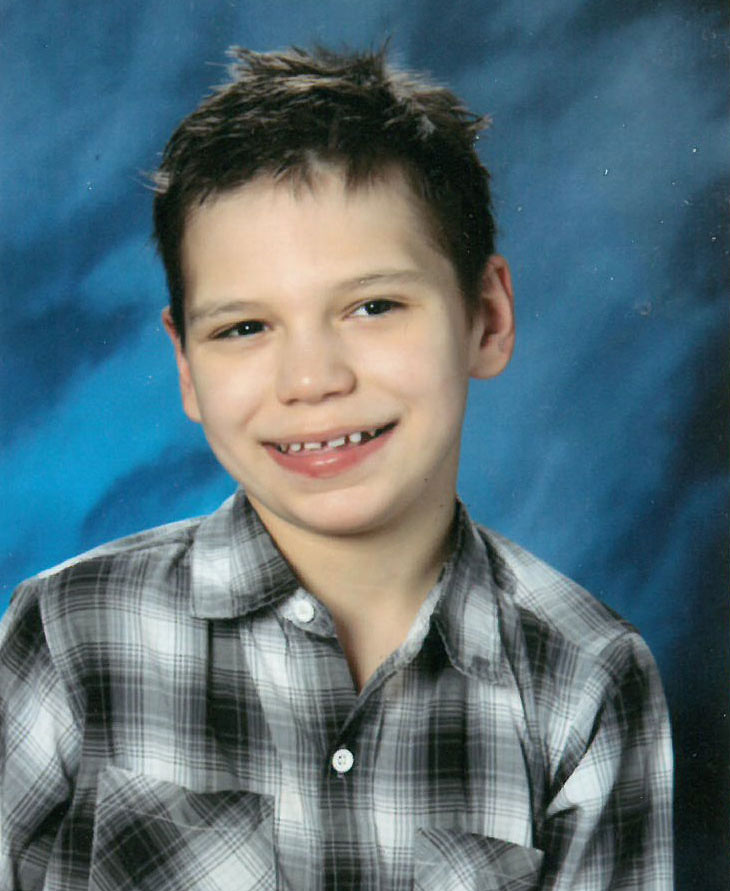 Boy in a black-and-white plaid shirt, looking sideways, smiles for his 7th grade school photo.
