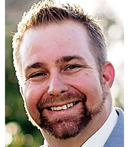 A White male with hazel eyes, brown hair, mustache and goatee.