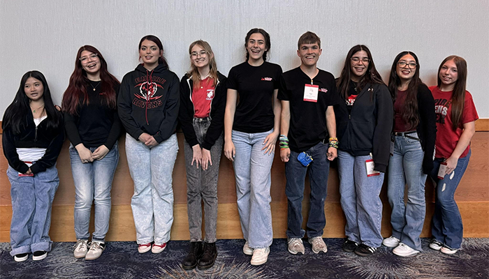 Nine young adults standing in a row indoors, wearing casual clothes.
