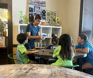 Children engaged in an activity around a table with a white shelf in the background.