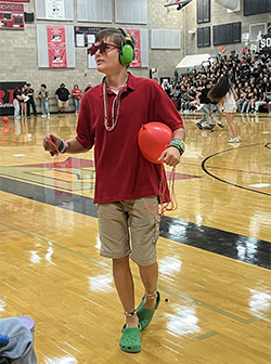 Person wearing a red shirt and green headphones holding a red balloon in a gymnasium.