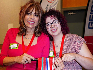 Two women smiling and holding several award medals.