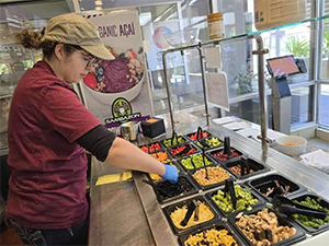 A worker preparing a dish at a food counter with various toppings.