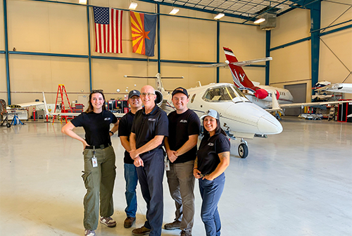 Five people standing in a hangar with an aircraft next to them.