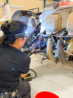A person working on an aircraft engine with a headlamp in a hangar.