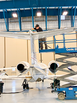 Technician working on the tail of a small jet inside a hangar.