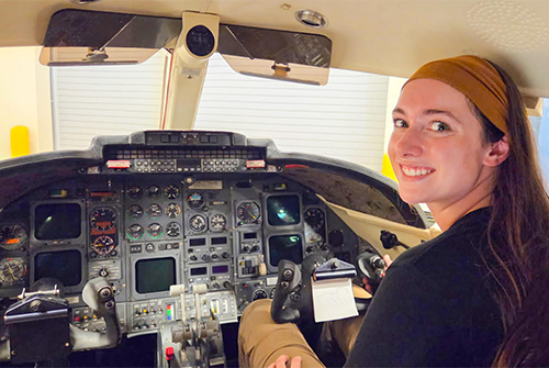 Person seated in an aircraft cockpit, smiling at the camera.
