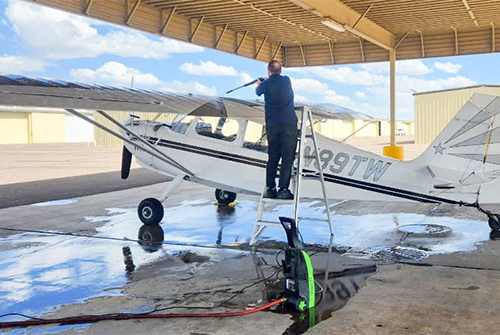 A person cleans the windshield of a small aircraft under a shelter.