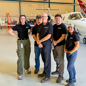 Five people standing in a hangar with an aircraft next to them