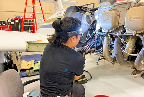 A person working on an aircraft engine with a headlamp in a hangar.