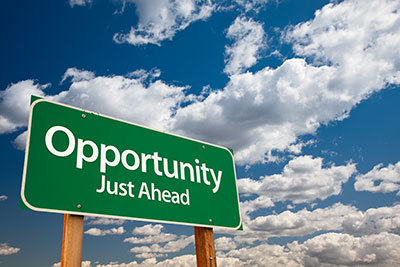 below blue sky with fluffy white clouds a billboard reads opportuniy just ahead