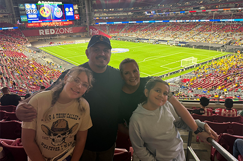 A family of four posing in a stadium with a soccer field in the background.