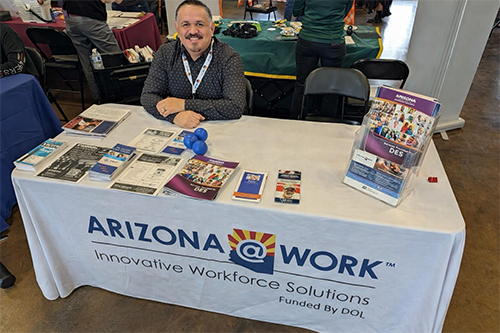 A person at an ARIZONA@WORK informational table with brochures and materials.