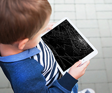 Young child holding a tablet with a broken screen.