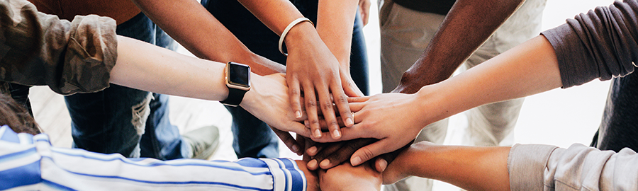 people standing in a circle, placing their hands forward in cooperation