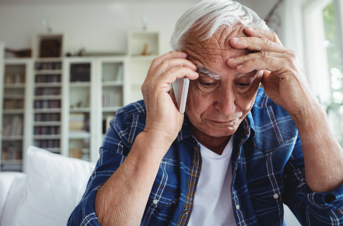 Concerned elderly man talking on the phone at home.