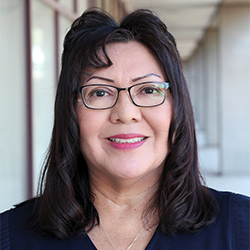 portrait of a person with shoulder length hair, wearing a dark top, and eyeglasses