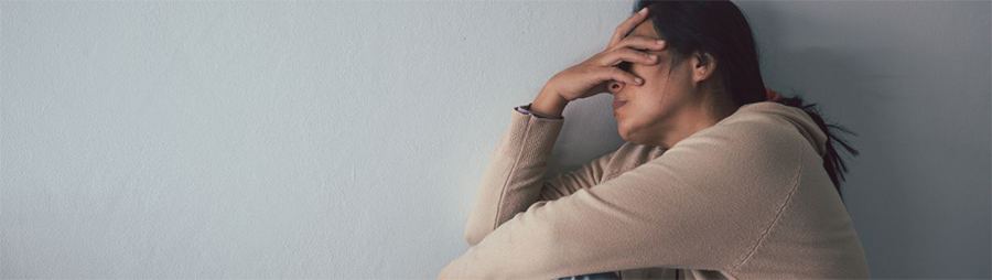 Person sitting against a blue wall, covering their face with one hand.