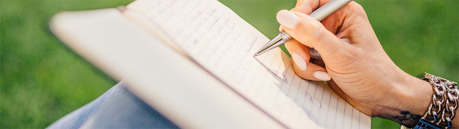 A hand writing in a notebook with blurred green background.