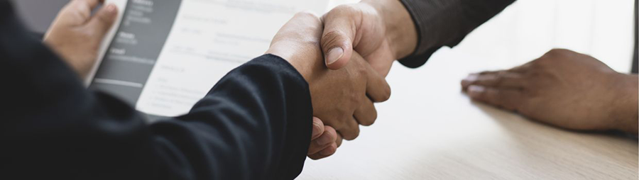 Close-up of a handshake across a light-colored table with a document.