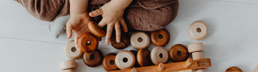 Child playing with round, flat wooden stacking toys on a light-colored floor.
