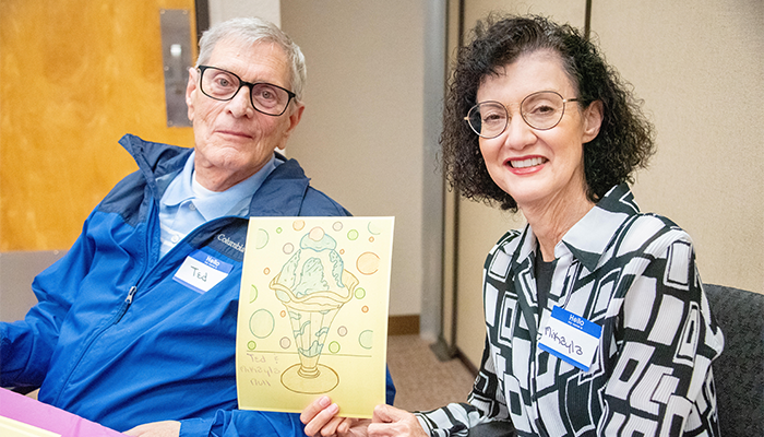 Two people holding a colorful drawing indoors.