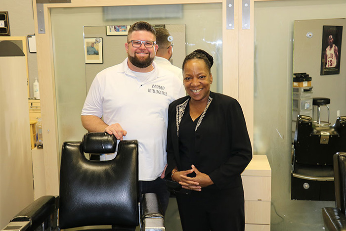 a man and a woman are standing inside a barbershop, smiling