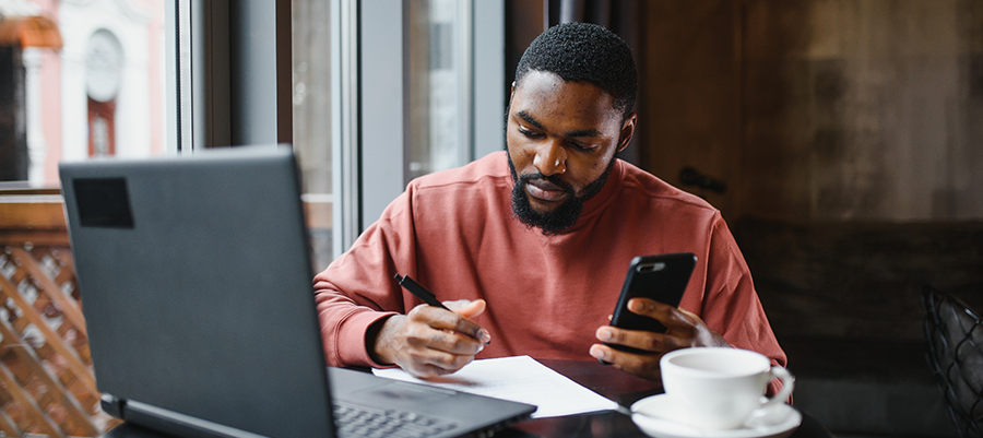 Man at desk writing and checking his phone.