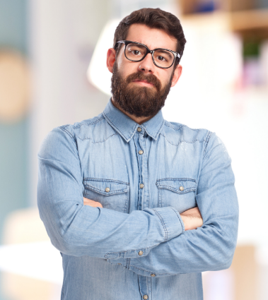 Man wearing a denim shirt with dark hair and a beard standing with his arms crossed.