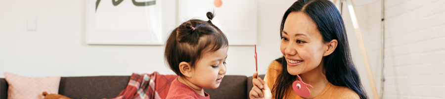 A smiling woman is holding up puppets made of popsicle sticks in front of a child.