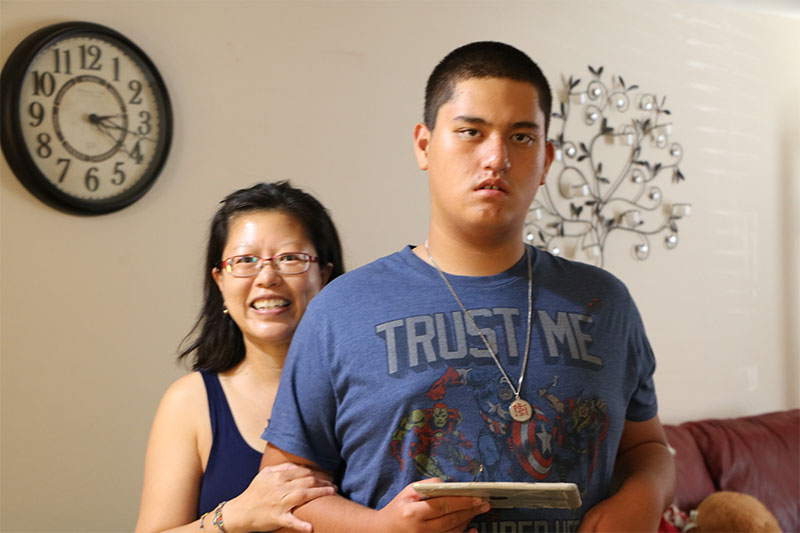 With her hand on his arm, a mother stands behind her teenage son in their East Valley living room.
