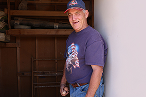 Middle-aged man wearing ball cap, T-shirt and blue jeans stands in the doorway of a chick house with two eggs in his right hand