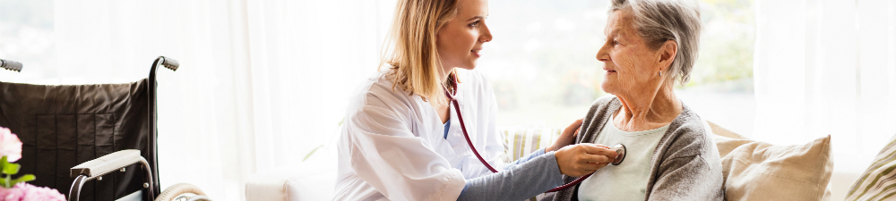 Nurse listening to patient's heartbeat with stethoscope in a home.