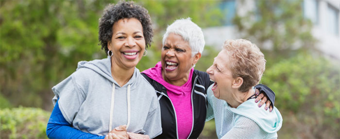 Three older women laugh and lean on each other